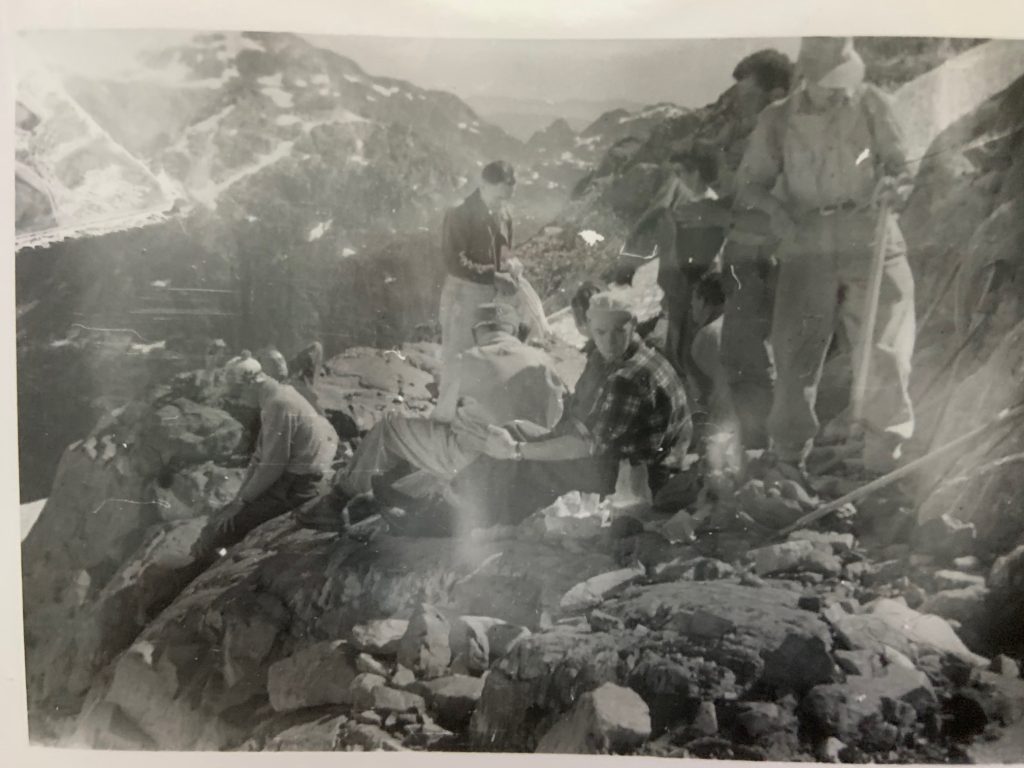 Lunch on Big Interior Mountain 1953. Geoffrey Capes on right with ice axe, Nigel Scott-Moncrief behind him. Rex Gibson sitting with back towards camera and Mark Mitchell standing beyond. – Syd Watts photo.