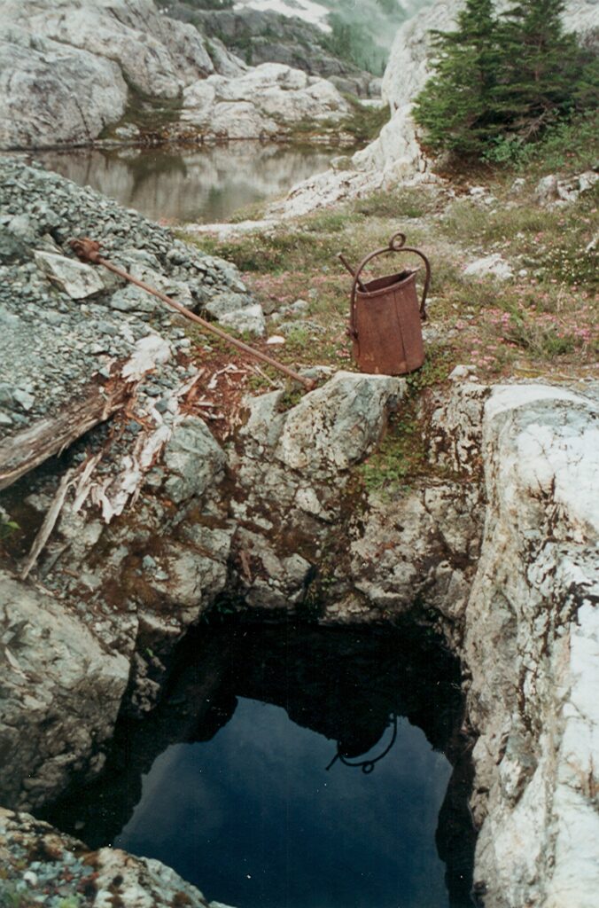An old mine shaft and an ore bucket on the shore of Della Lake 1994 – Lindsay Elms photo